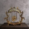 Handcrafted brass Ganesha jhula idol showing Lord Ganpati seated on an ornate swing suspended from a peacock arch with hanging bells. Antique golden finish with intricate filigree details. Perfect for pooja room and spiritual home decor.