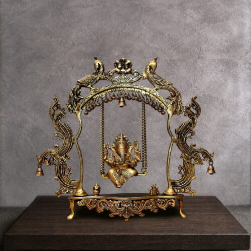 Handcrafted brass Ganesha jhula idol showing Lord Ganpati seated on an ornate swing suspended from a peacock arch with hanging bells. Antique golden finish with intricate filigree details. Perfect for pooja room and spiritual home decor.