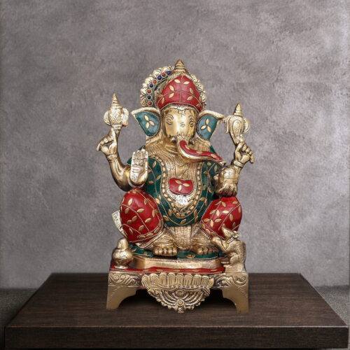 Handcrafted brass Lord Ganesha idol with traditional red and green Meenakari artwork, seated on an ornate pedestal for home temple and luxury interior décor.