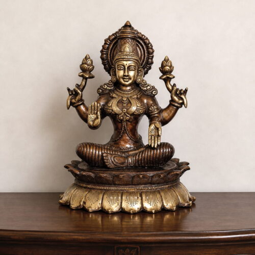 Premium handcrafted Brass Goddess Lakshmi Idol seated on a lotus pedestal with intricate temple-style carvings, antique dual-tone finish, and lotus flowers for home temple, Diwali Puja, Vaastu, and luxury spiritual décor.