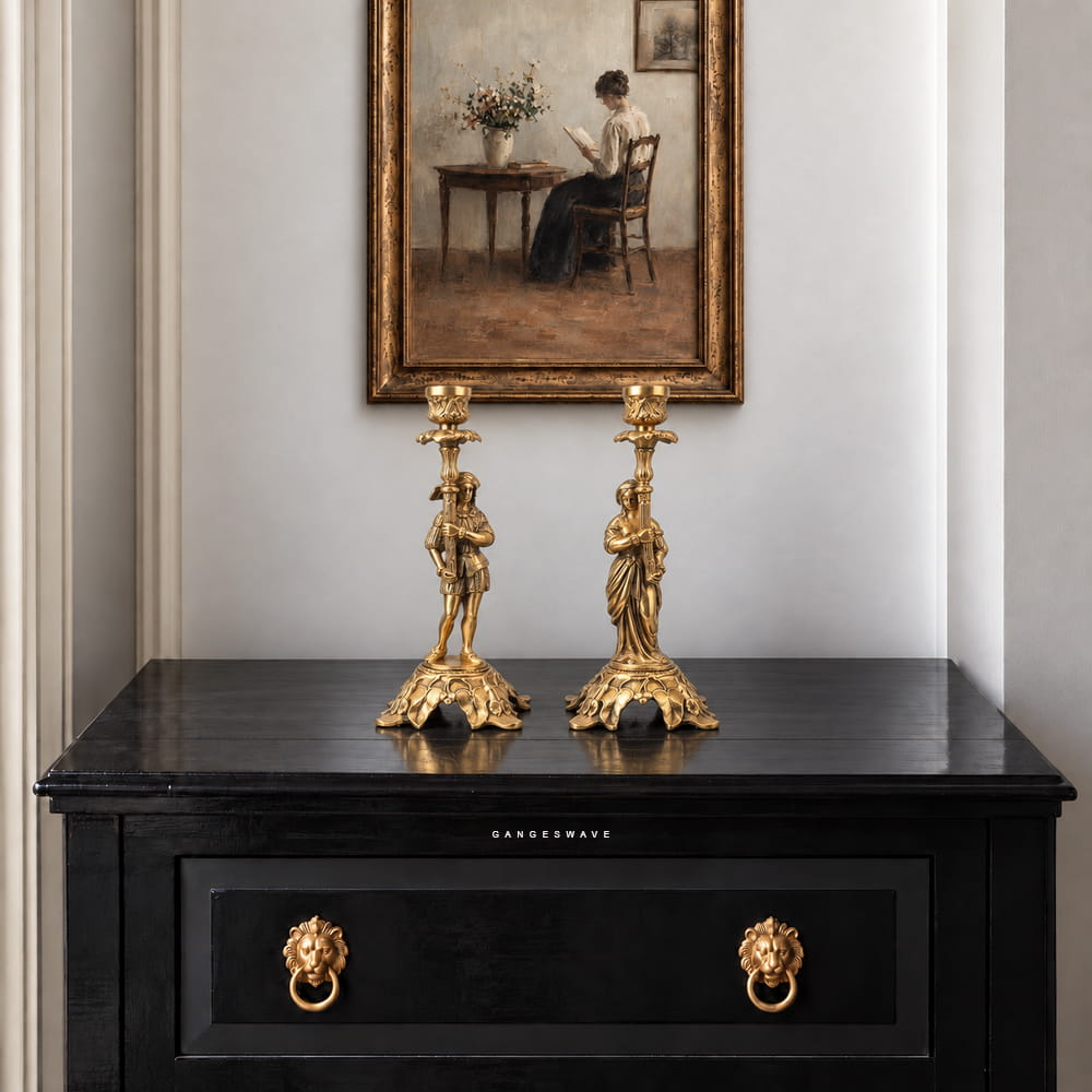 Pair of vintage brass figurine candle holders with ornate bases and golden finish displayed on a dark console.